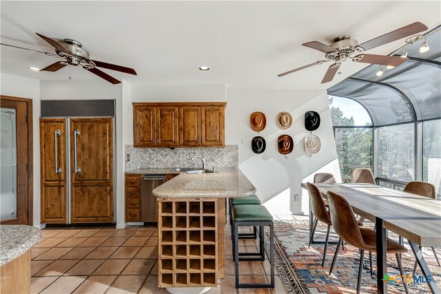 kitchen with a sink, a sunroom, backsplash, dishwasher, and brown cabinetry