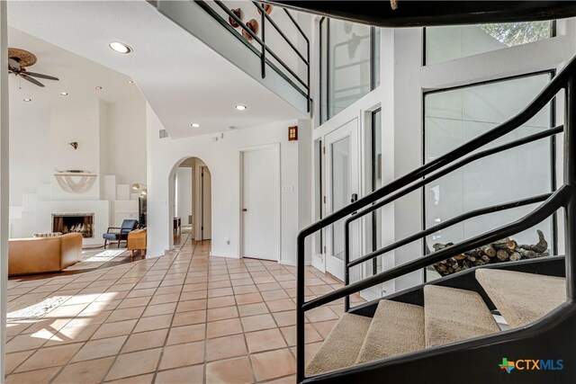 2701 Hillside Cir, New Braunfels, TX 78132 - staircase featuring arched walkways, a high ceiling, tile patterned flooring, a fireplace with raised hearth, and a ceiling fan