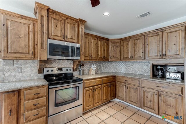 2701 Hillside Cir, New Braunfels, TX 78132 - kitchen featuring stainless steel appliances, tasteful backsplash, light tile patterned flooring, light stone countertops, and brown cabinetry