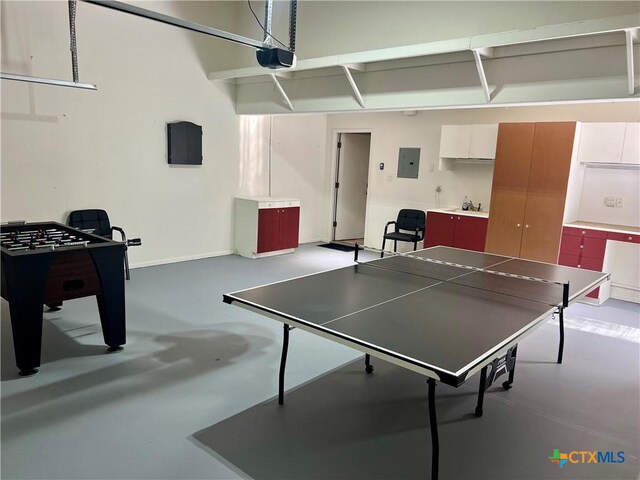 rec room with concrete flooring, a sink, a garage, electric panel, and baseboards