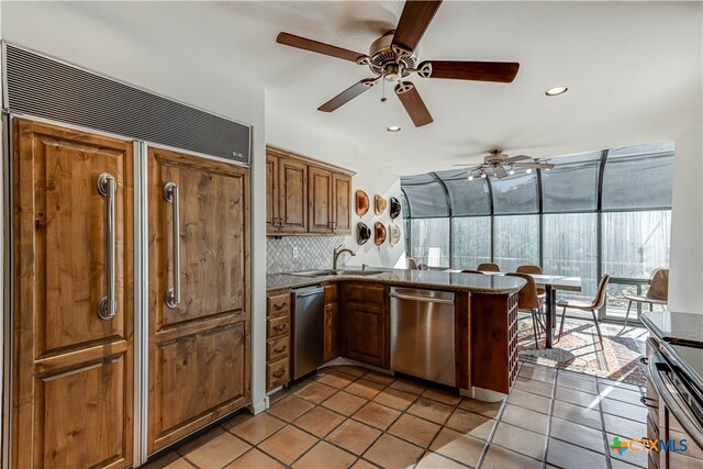 kitchen with light tile patterned floors, stainless steel appliances, a peninsula, a sink, and tasteful backsplash