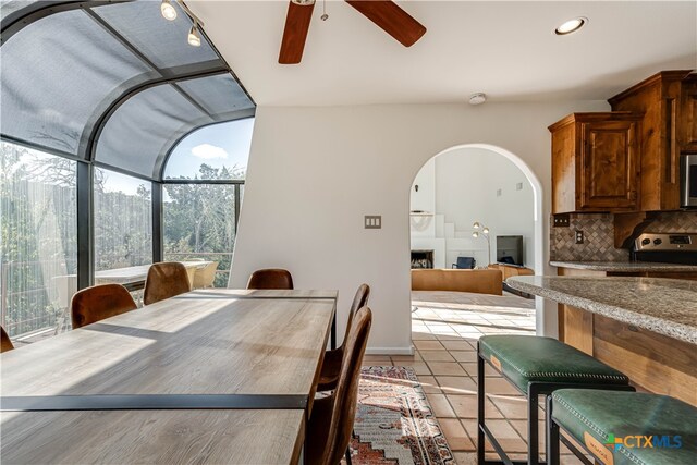 dining space featuring a ceiling fan, a sunroom, light tile patterned flooring, a fireplace, and recessed lighting