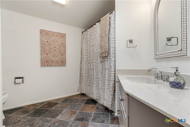 bathroom with toilet, stone finish flooring, baseboards, and vanity