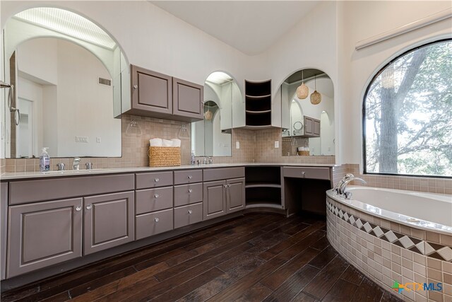 full bathroom with a sink, wood finished floors, a bath, decorative backsplash, and double vanity