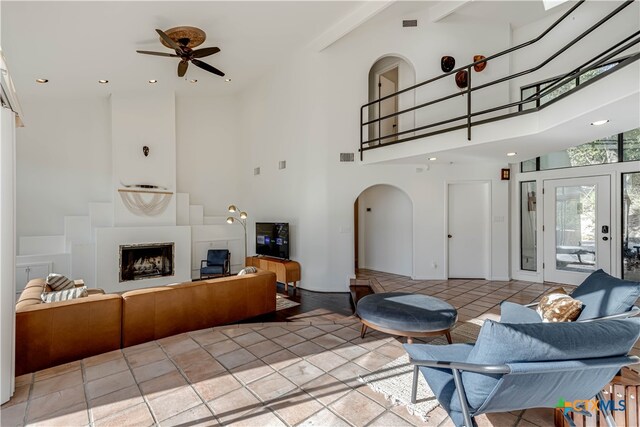 living room featuring arched walkways, a fireplace, visible vents, a towering ceiling, and ceiling fan