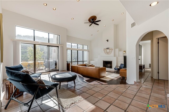 living area featuring a fireplace with raised hearth, high vaulted ceiling, arched walkways, recessed lighting, and tile patterned floors