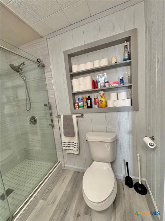 bathroom with built in shelves, toilet, an enclosed shower, and hardwood / wood-style flooring