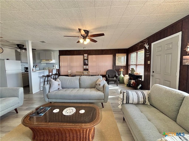 living room featuring wooden walls, ceiling fan, and light hardwood / wood-style floors