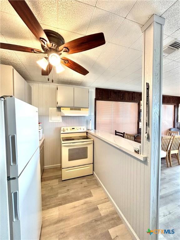 kitchen featuring ceiling fan, wood walls, white appliances, and light hardwood / wood-style floors