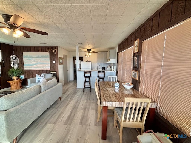 dining space featuring ceiling fan, wooden walls, and light wood-type flooring