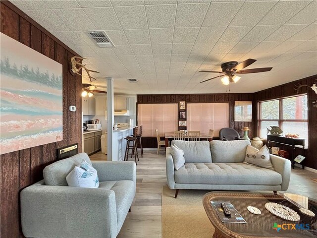 living room featuring ceiling fan, light hardwood / wood-style flooring, and wood walls