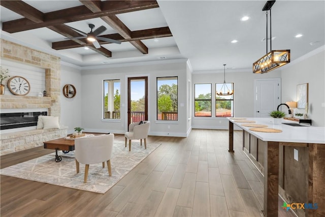 living room with a stone fireplace, coffered ceiling, light wood-type flooring, and plenty of natural light