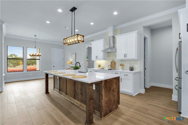 kitchen featuring hanging light fixtures, a kitchen breakfast bar, white cabinets, a center island with sink, and wall chimney exhaust hood