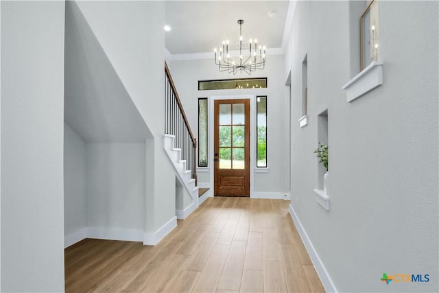 entrance foyer featuring a notable chandelier, ornamental molding, and light wood-type flooring