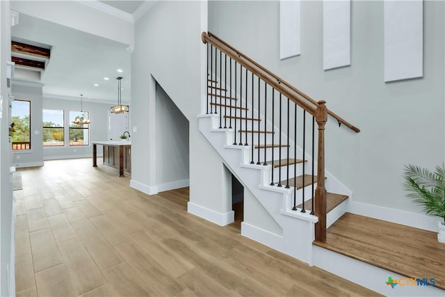 stairs with crown molding, a towering ceiling, hardwood / wood-style floors, and an inviting chandelier