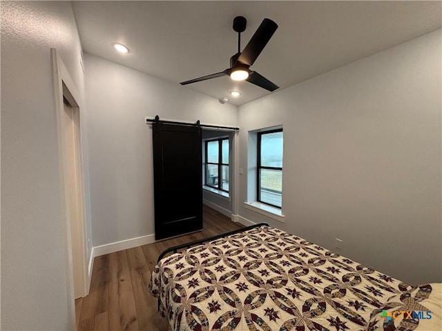 bedroom featuring ceiling fan, a barn door, and dark hardwood / wood-style flooring