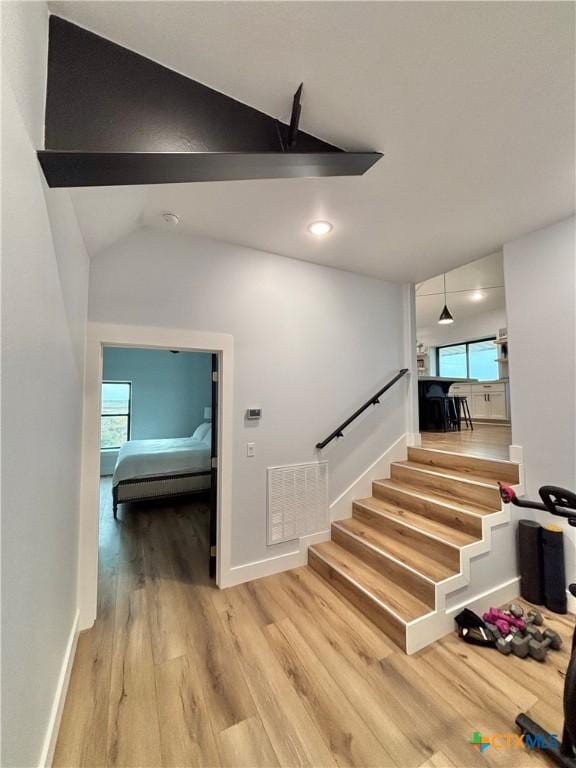 stairway with lofted ceiling, a healthy amount of sunlight, and hardwood / wood-style floors