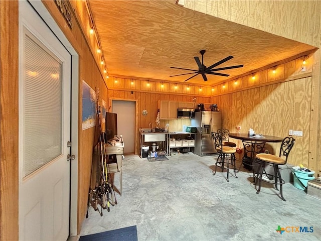 interior space featuring ceiling fan, appliances with stainless steel finishes, track lighting, kitchen peninsula, and wood walls