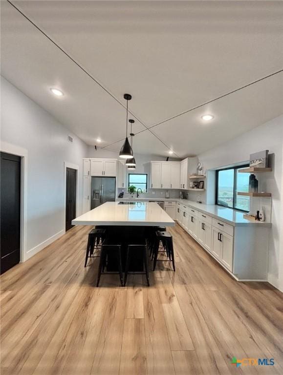 kitchen with a spacious island, a breakfast bar area, black fridge, white cabinetry, and decorative light fixtures