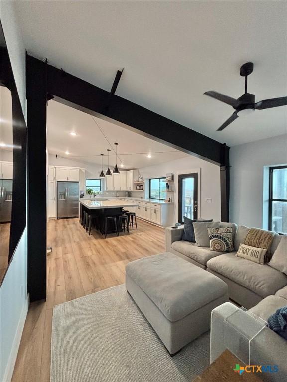 living room featuring ceiling fan, light hardwood / wood-style floors, and beamed ceiling