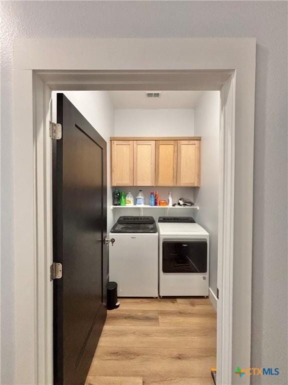 clothes washing area featuring cabinets, washing machine and dryer, and light hardwood / wood-style floors