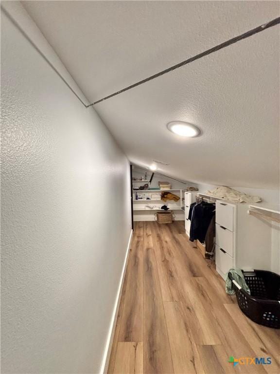 hallway with lofted ceiling, light hardwood / wood-style flooring, and a textured ceiling