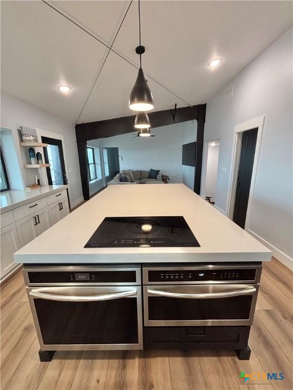 kitchen with vaulted ceiling, pendant lighting, white cabinetry, stainless steel oven, and black electric stovetop