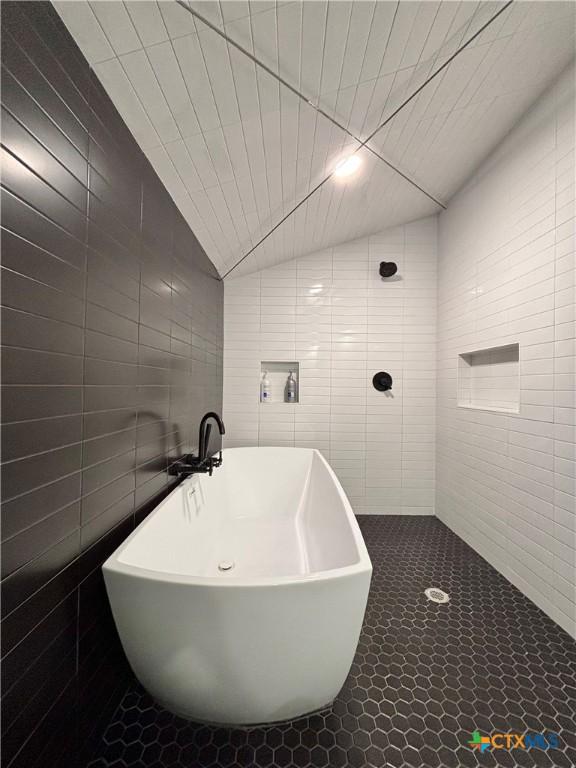 bathroom with tile walls, a bath, tile patterned flooring, and vaulted ceiling