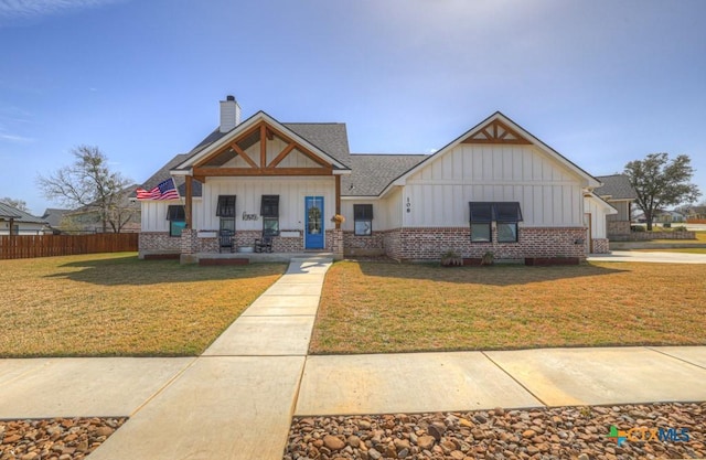 view of front of home featuring a front yard, fence, brick siding, a chimney, and board and batten siding