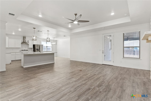 unfurnished living room featuring crown molding, light hardwood / wood-style flooring, ceiling fan, and a tray ceiling