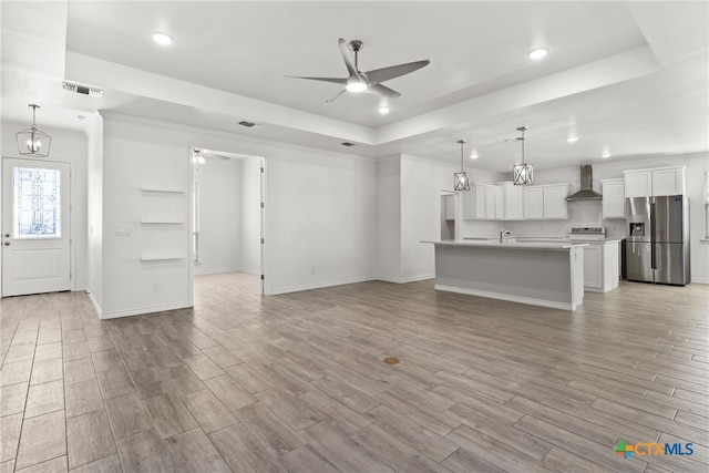 unfurnished living room featuring a tray ceiling and ceiling fan with notable chandelier