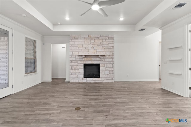 unfurnished living room with ceiling fan, ornamental molding, a tray ceiling, and a stone fireplace