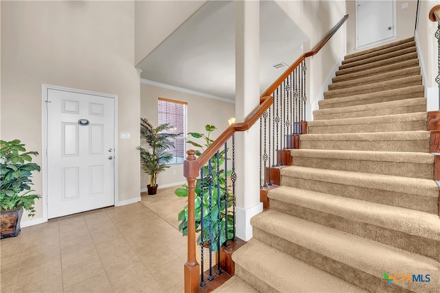 foyer entrance featuring crown molding, light tile patterned floors, and a high ceiling