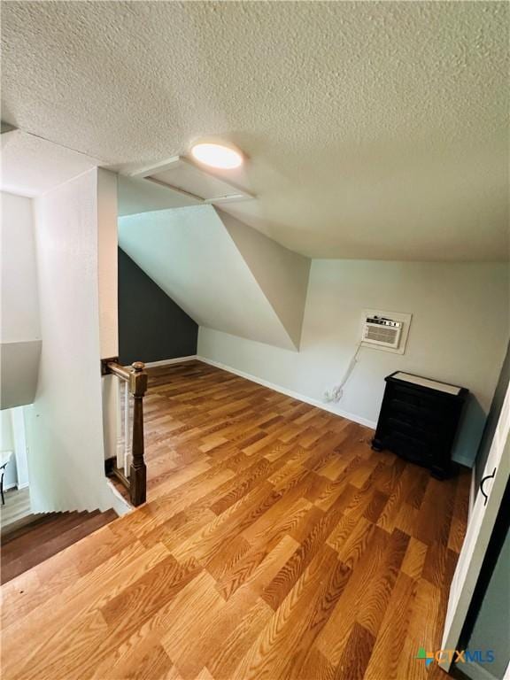 bonus room with hardwood / wood-style floors, a textured ceiling, and a wall mounted AC