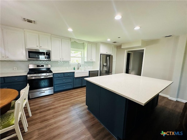 kitchen featuring white cabinets, blue cabinets, sink, appliances with stainless steel finishes, and a kitchen island