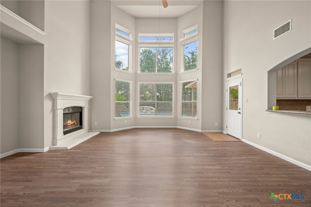 1018 Canyon Maple Rd, Pflugerville, TX 78660 - unfurnished living room with a high ceiling, healthy amount of natural light, a lit fireplace, and wood finished floors