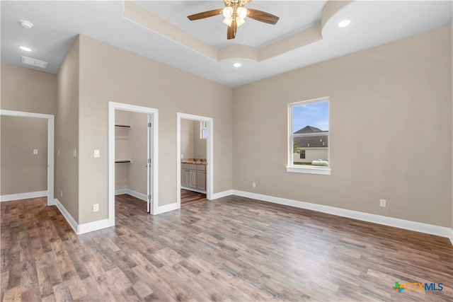 unfurnished bedroom with ceiling fan, connected bathroom, a walk in closet, and wood-type flooring