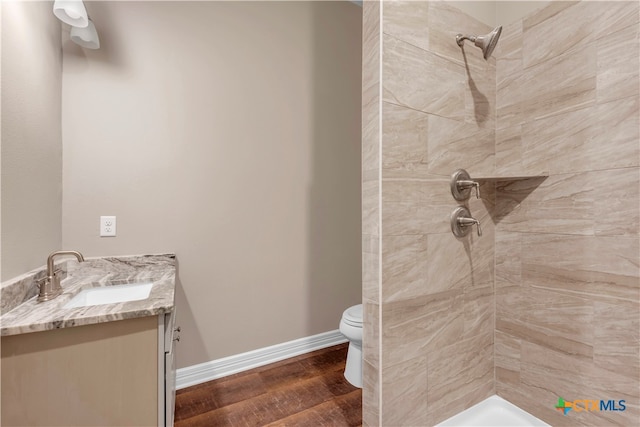 bathroom with toilet, vanity, hardwood / wood-style floors, and tiled shower