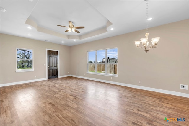 unfurnished room with hardwood / wood-style flooring, ceiling fan with notable chandelier, and a raised ceiling