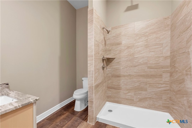 bathroom with toilet, vanity, wood-type flooring, and tiled shower