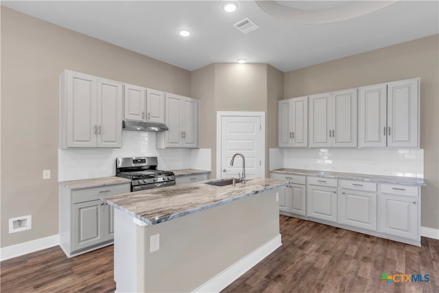 kitchen with dark wood-type flooring, stainless steel gas range oven, a center island with sink, and white cabinetry