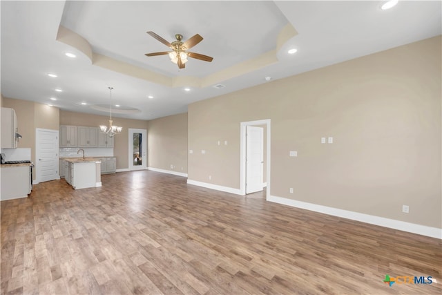 unfurnished living room featuring ceiling fan with notable chandelier, light hardwood / wood-style flooring, and a tray ceiling