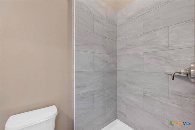 bathroom featuring tiled shower and toilet