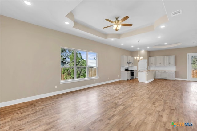 unfurnished living room with ceiling fan with notable chandelier, light hardwood / wood-style flooring, sink, and a tray ceiling