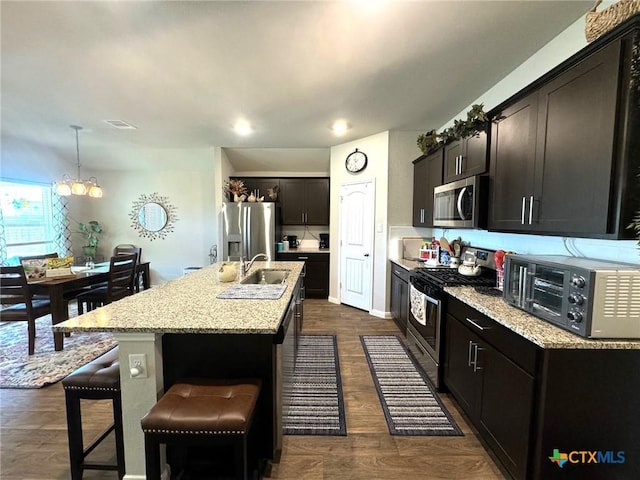 kitchen featuring appliances with stainless steel finishes, a center island with sink, decorative light fixtures, a chandelier, and dark hardwood / wood-style floors