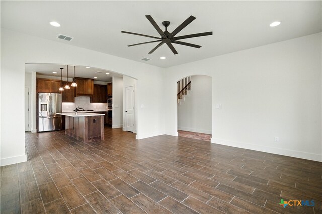 unfurnished living room with visible vents, arched walkways, dark wood finished floors, and a ceiling fan