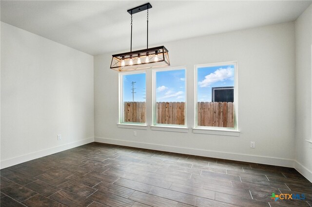 unfurnished dining area with a chandelier, baseboards, and dark wood finished floors