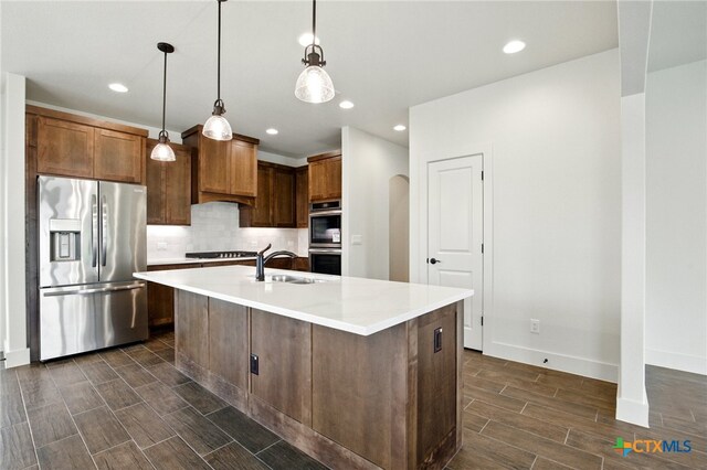 kitchen with wood finish floors, appliances with stainless steel finishes, a sink, light countertops, and backsplash