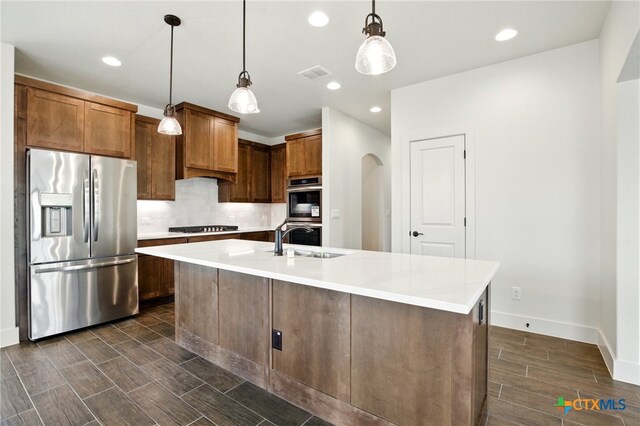 kitchen with a sink, stainless steel appliances, wood tiled floor, backsplash, and visible vents