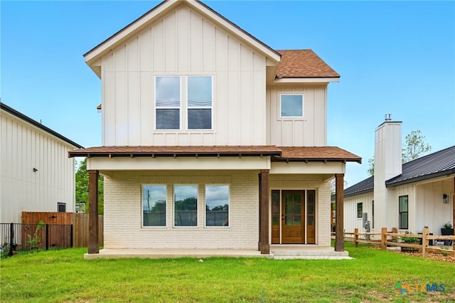 rear view of house with brick siding, board and batten siding, fence, and a lawn